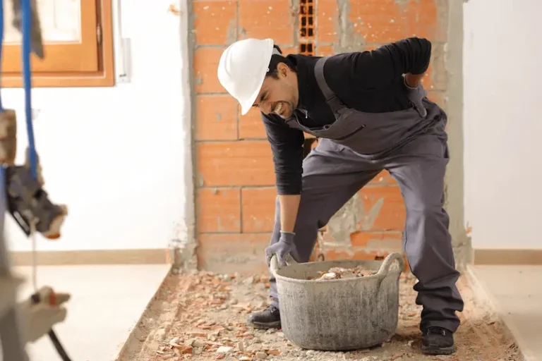 A construction worker leans over in pain from being injured on the job due to lifting.